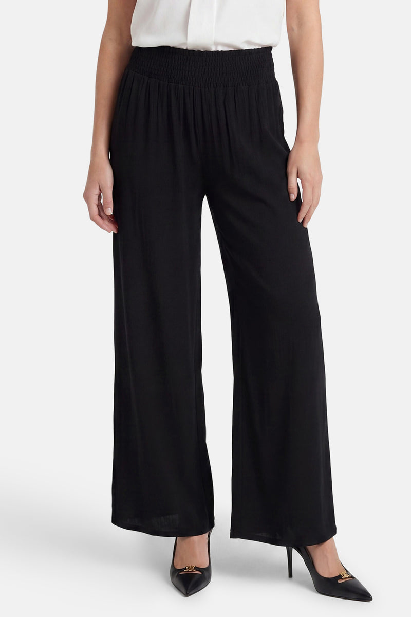 Black elastic waist wide-leg trousers with smocked waistband, worn with white top and black heels, front view