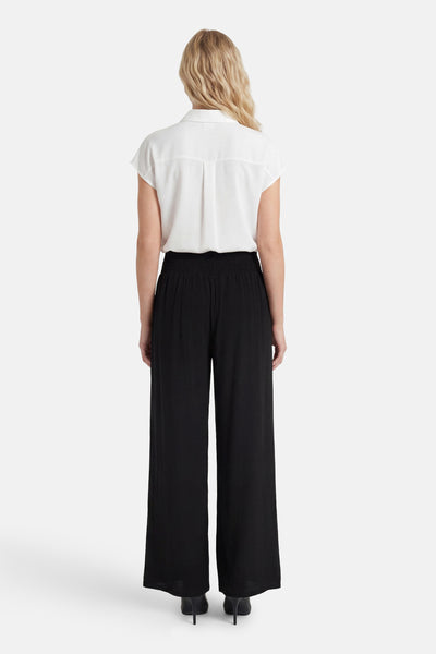 Black wide-leg elastic waist trousers with ribbed texture, back view, worn with white blouse and black heels