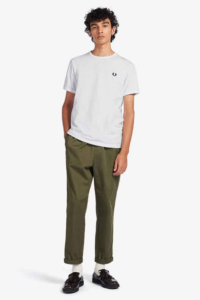 T-shirt blanc à manches courtes de Fred Perry, porté avec un pantalon vert olive retroussé et des mocassins.