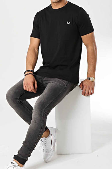 T-shirt noir FRED PERRY à manches courtes par Fred Perry, porté avec un jean gris et des baskets blanches.