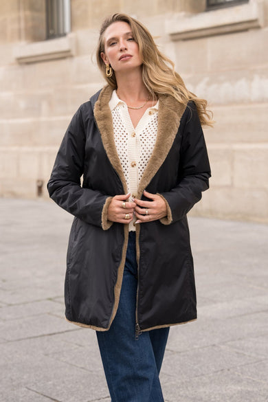 Imperméable noir de LAURA JO avec garniture en fausse fourrure, porté avec un cardigan crème et un jean bleu.