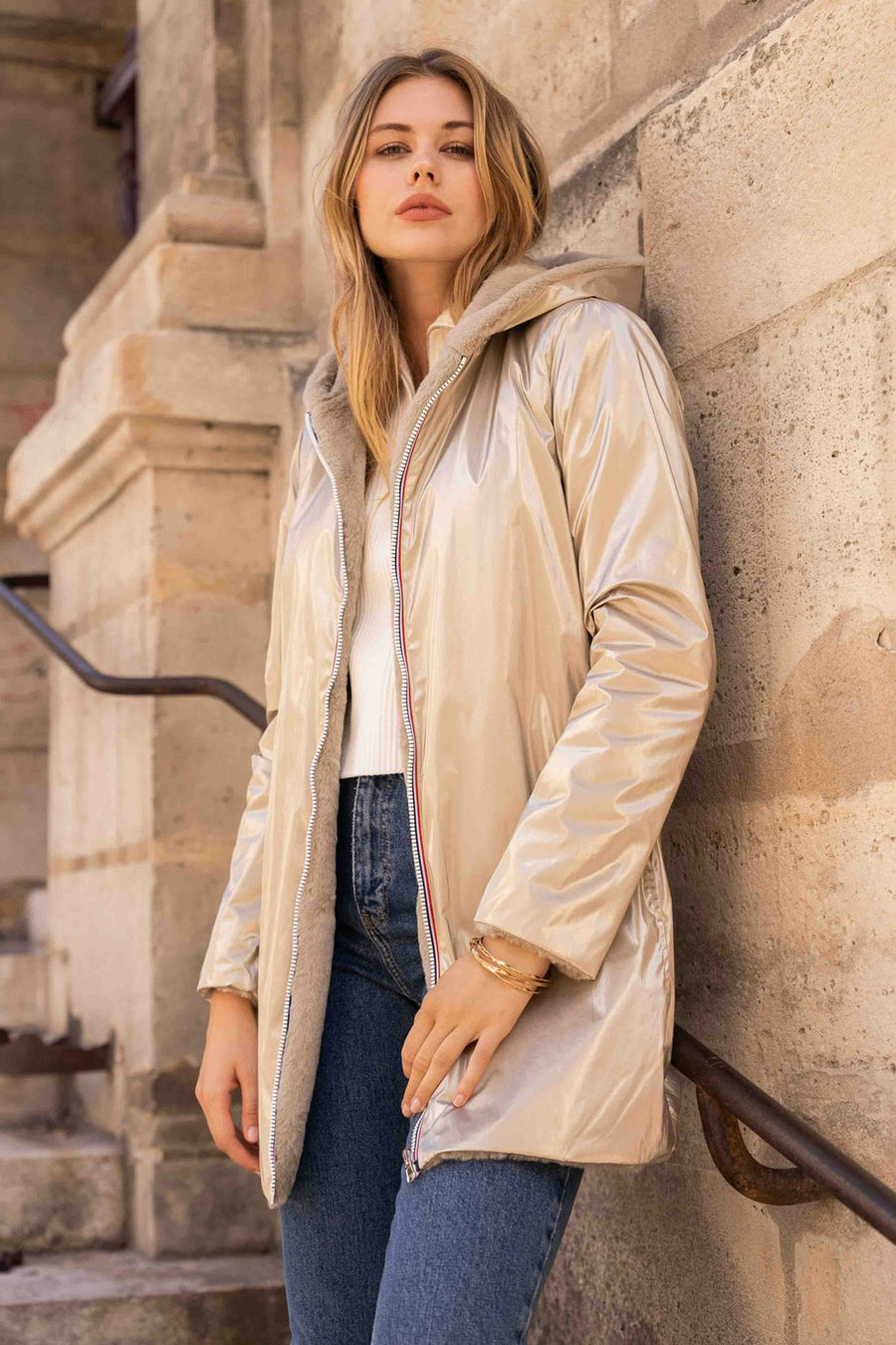 Gouden regenjas van LAURA JO met imitatiebontvoering, gedragen met een witte trui en een blauwe jeans.