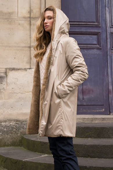 Imperméable beige de LAURA JO avec capuche bordée de fourrure, porté avec un pull en maille et un pantalon sombre.