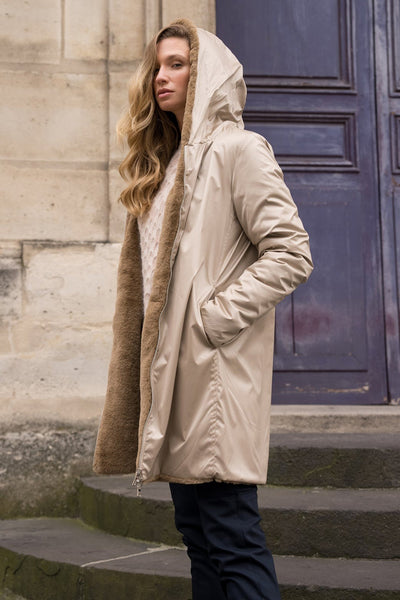 Imperméable beige de LAURA JO avec capuche bordée de fourrure, porté avec un pull en maille et un pantalon sombre.