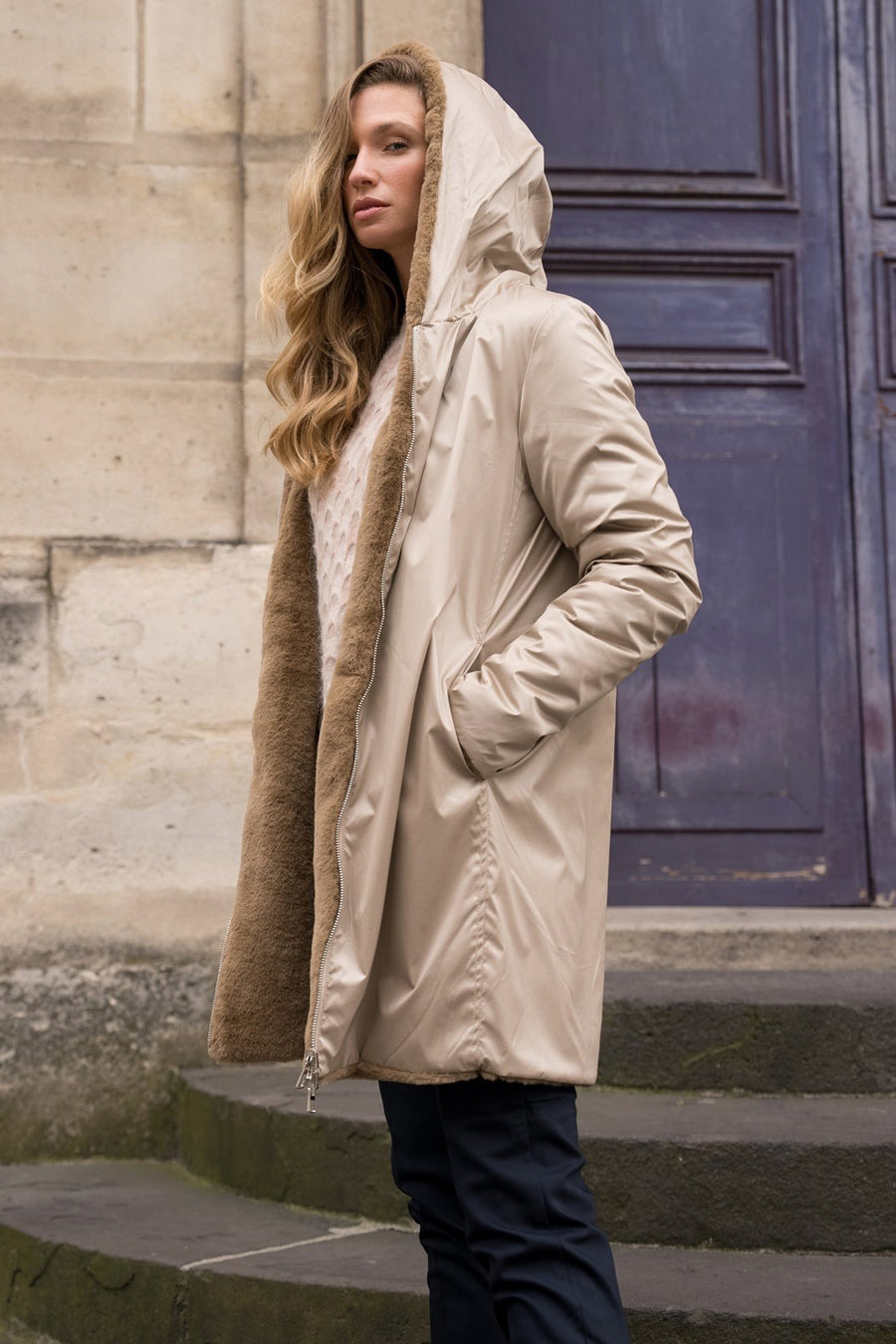 Imperméable beige de LAURA JO avec capuche bordée de fourrure, porté avec un pull en maille et un pantalon sombre.