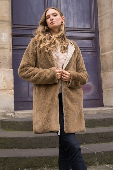 Beige regenjas van LAURA JO met een lichte voering, gedragen met een marineblauwe broek en gouden sieraden.