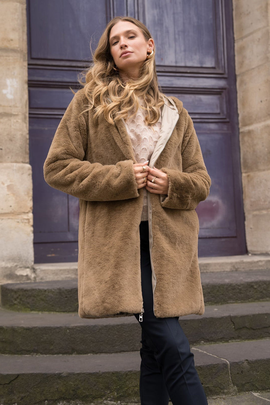Beige regenjas van LAURA JO met een lichte voering, gedragen met een marineblauwe broek en gouden sieraden.