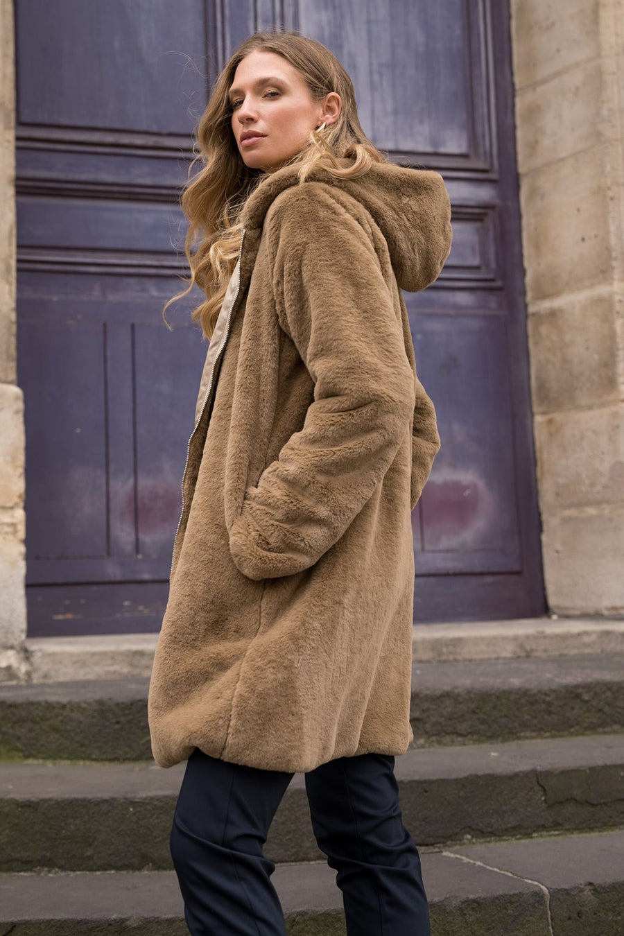 Beige regenjas van LAURA JO met capuchon, gedragen met een donkere broek, zijwaarts gezien.