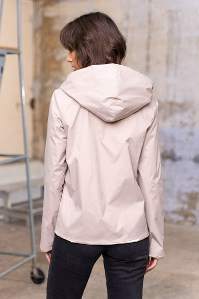Veste de pluie beige par LAURA JO, vue de dos, avec une capuche et portée avec un jean noir.