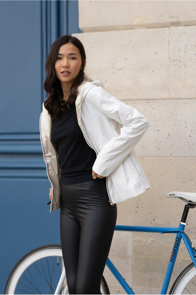 Ecru regenjas van LAURA JO, gedragen met een zwart T-shirt, een leren legging, sneakers en een blauwe fiets.