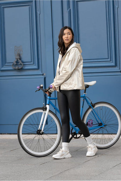 Ecru regenjas van LAURA JO, gedragen met een zwarte legging en witte sneakers, voor een blauwe deur.
