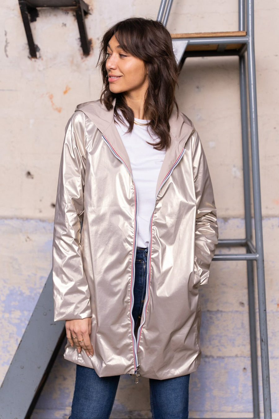 Beige regenjas van LAURA JO met capuchon, gedragen over een wit T-shirt en een blauwe jeans.