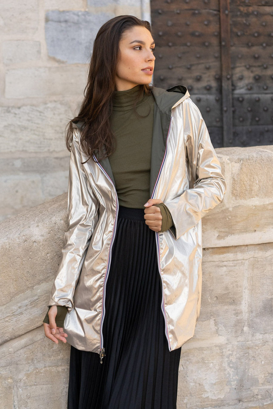 Imperméable vert de LAURA JO, avec un extérieur argenté brillant, porté avec un col roulé et une jupe plissée noire.