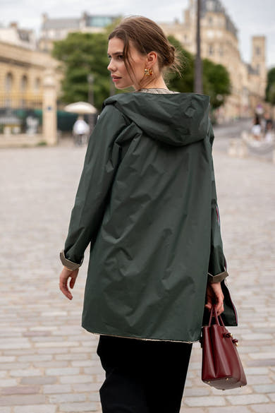 Olijfgroene regenjas van LAURA JO met capuchon, gedragen met een zwarte broek en een bordeauxrode handtas.