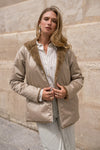 Beige regenjas van LAURA JO gedragen met een gestreept overhemd en een gestreepte broek, met een witte handtas vast.