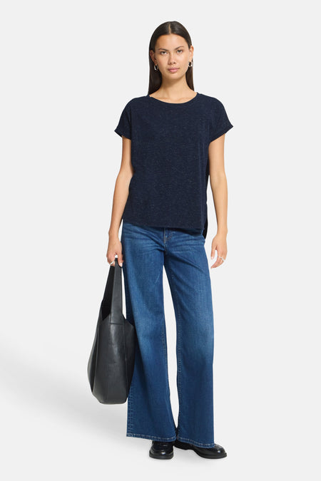 Navy blue short-sleeve t-shirt with subtle speckled texture, worn with wide-leg jeans and black tote bag, front view.
