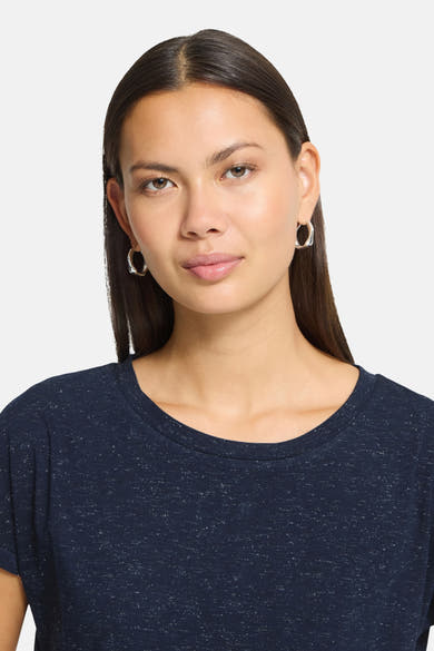 Navy blue short-sleeve t-shirt with speckled texture, round neckline, worn by model with silver hoop earrings, front view close-up