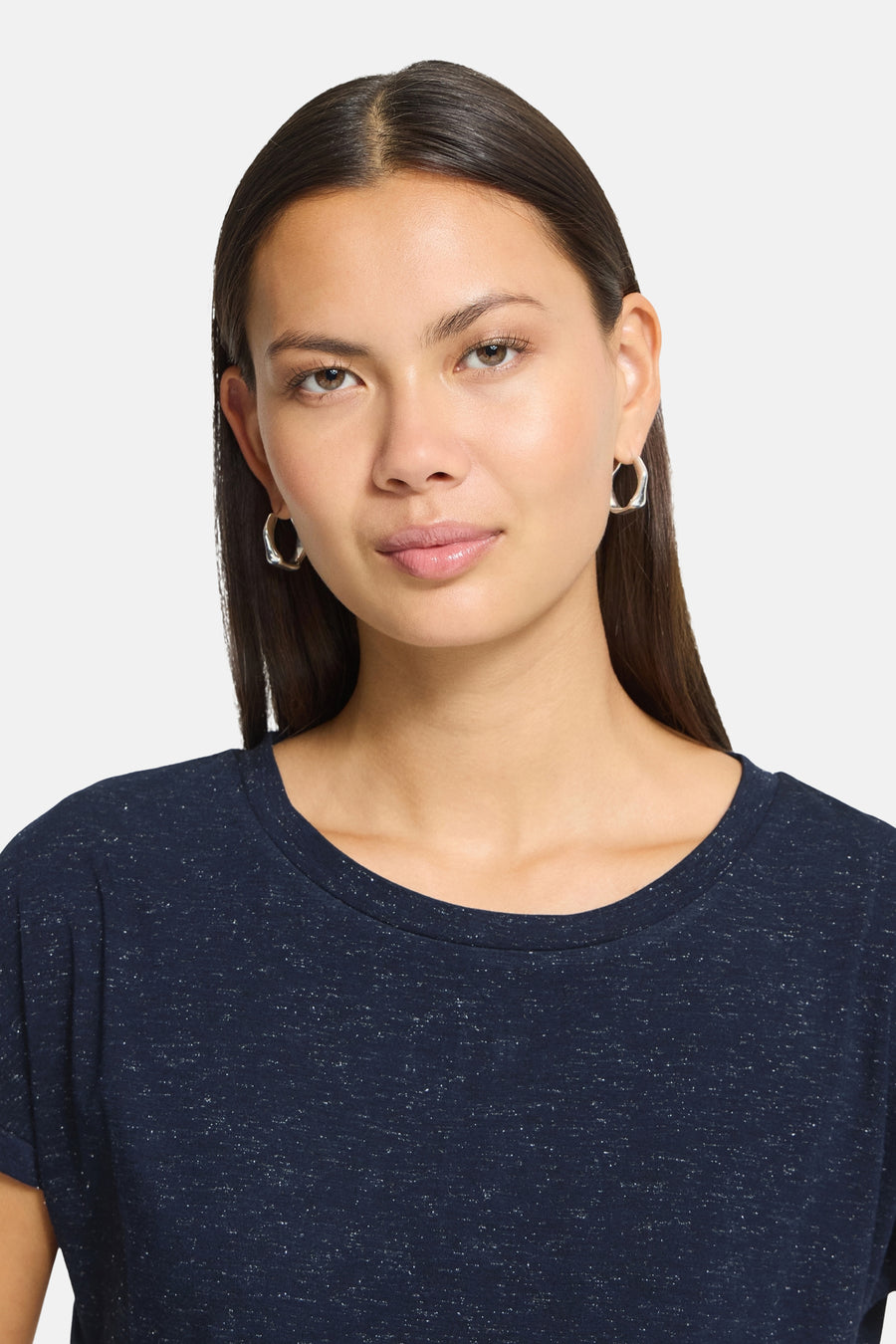 Navy blue short-sleeve t-shirt with speckled texture, round neckline, worn by model with silver hoop earrings, front view close-up