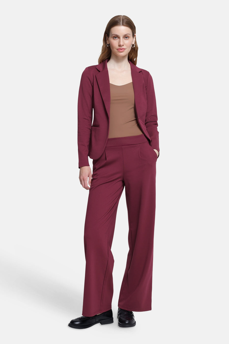 Burgundy wide-leg trousers with high waist and clean front pleats, worn with matching blazer, brown top, and black loafers in full-length lifestyle view