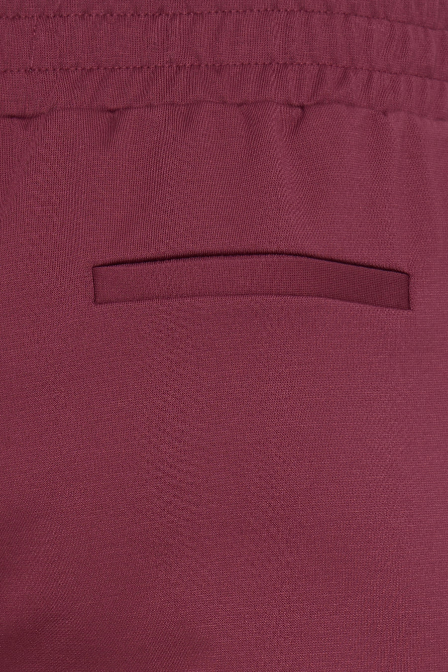 Red knit pants with elastic waistband and side pocket, close-up view showing textured fabric detail