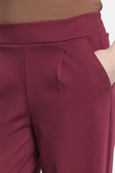 Burgundy high-waisted trousers with elastic waistband and front pleats, cropped side view showing smooth texture and pocket detail