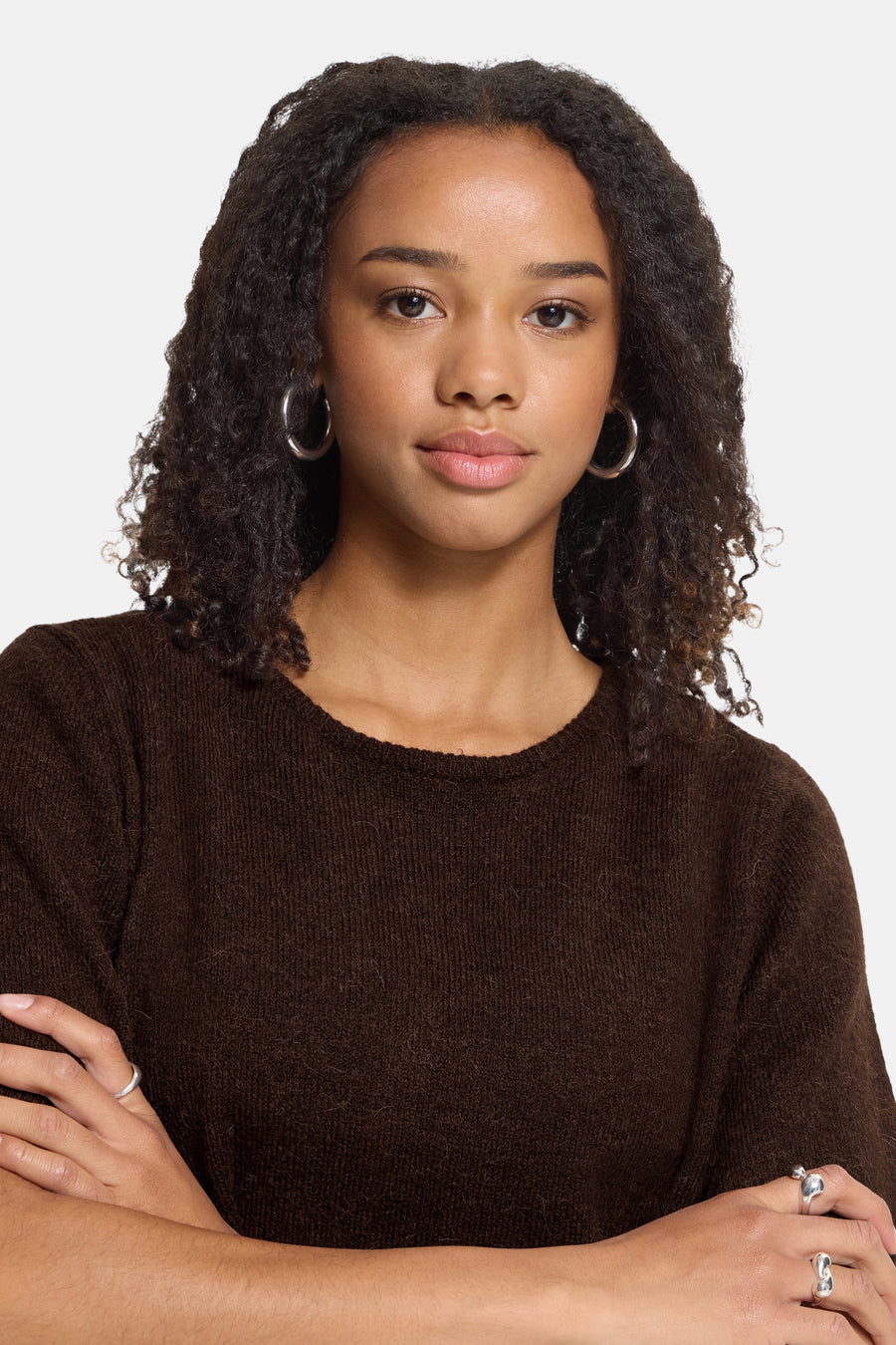Brown crewneck sweater with soft knit texture, worn by model with curly hair and silver hoop earrings, front view