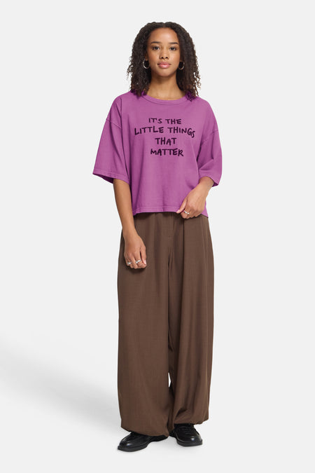 Rose oversized short-sleeve t-shirt with black text graphic, worn with brown wide-leg pants and black shoes, front view.