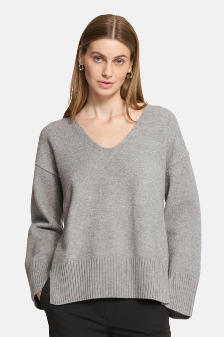 Grey V-neck sweater with ribbed hem and cuffs, worn by model in front view, soft knit texture, relaxed fit