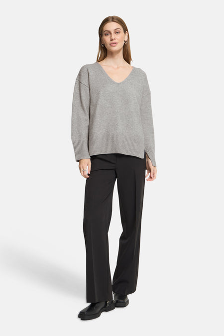 Grey V-neck sweater with ribbed hem and cuffs, worn with black trousers and chunky boots, full-length front view.