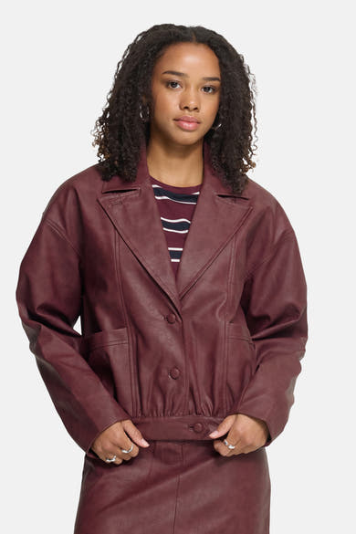 Burgundy faux leather vest by ICHI, featuring wide lapels, front buttons, and waist belt, worn with striped top, front view.
