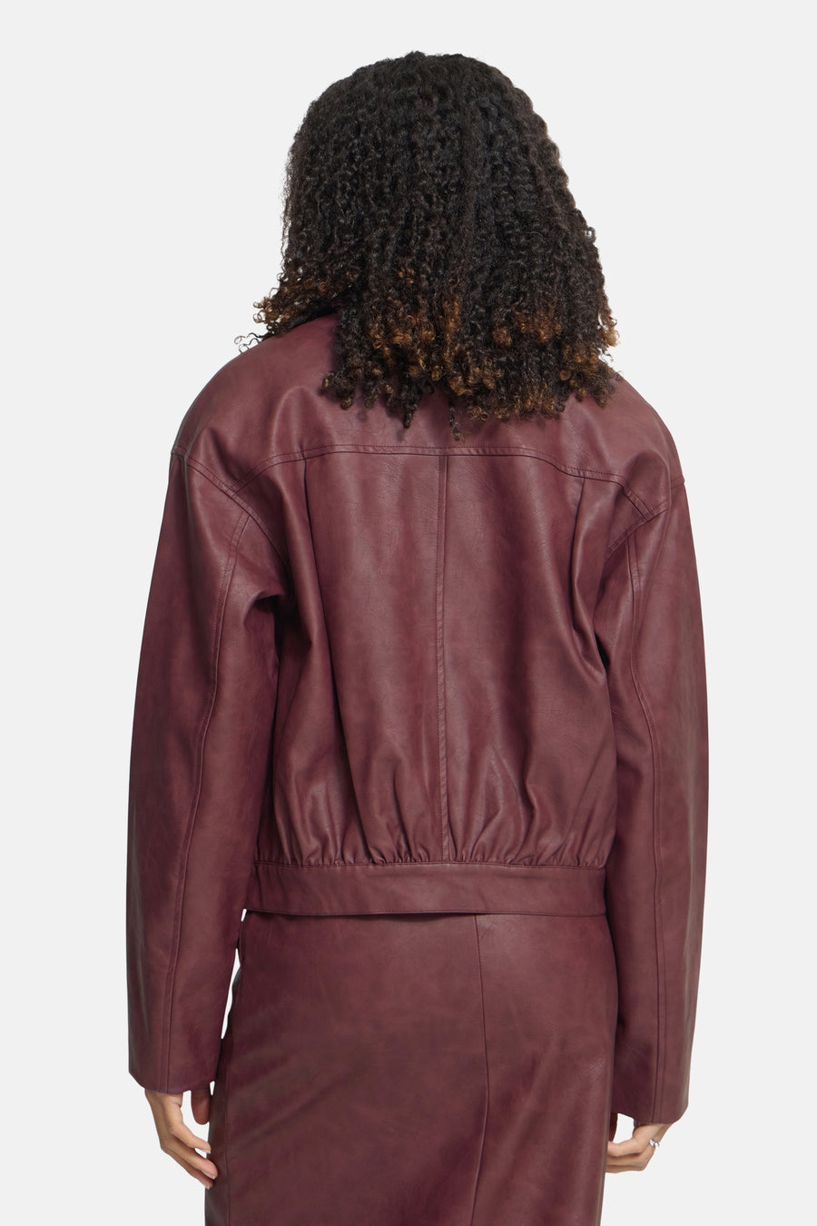 Burgundy faux leather jacket by ICHI, back view with gathered waist and long sleeves, worn with matching skirt.
