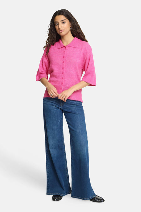 Rose pink knitted gilet with button front and collar, worn with wide-leg jeans and black loafers, full-length lifestyle view.