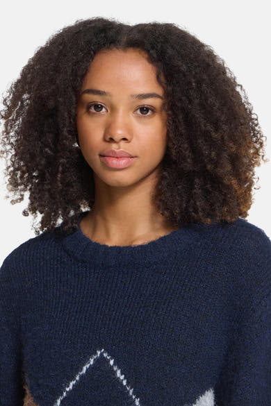 Navy blue crewneck sweater with white geometric pattern and textured knit, front view on model with curly hair
