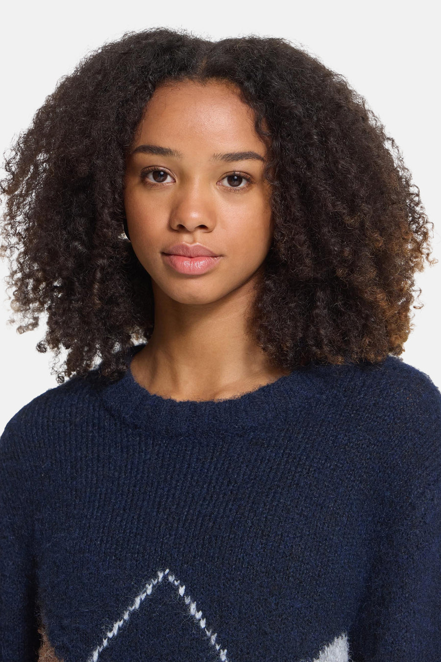 Navy blue crewneck sweater with white geometric pattern and textured knit, front view on model with curly hair