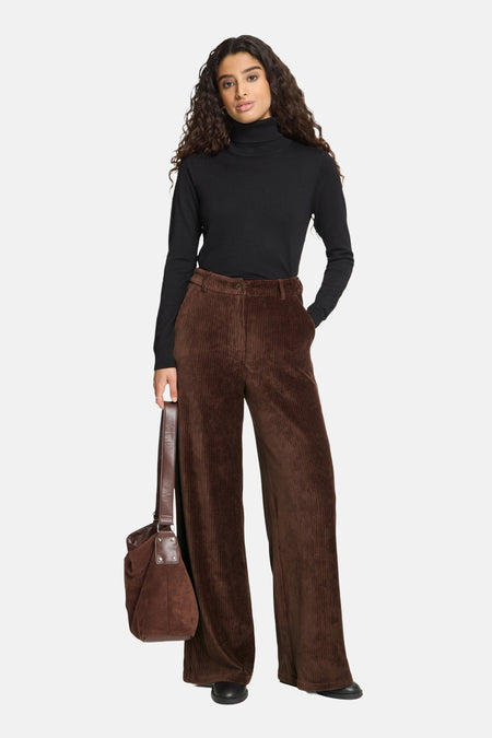 Brown corduroy wide-leg suit pants by ICHI, featuring ribbed texture and high waist, worn with black turtleneck and brown tote bag.
