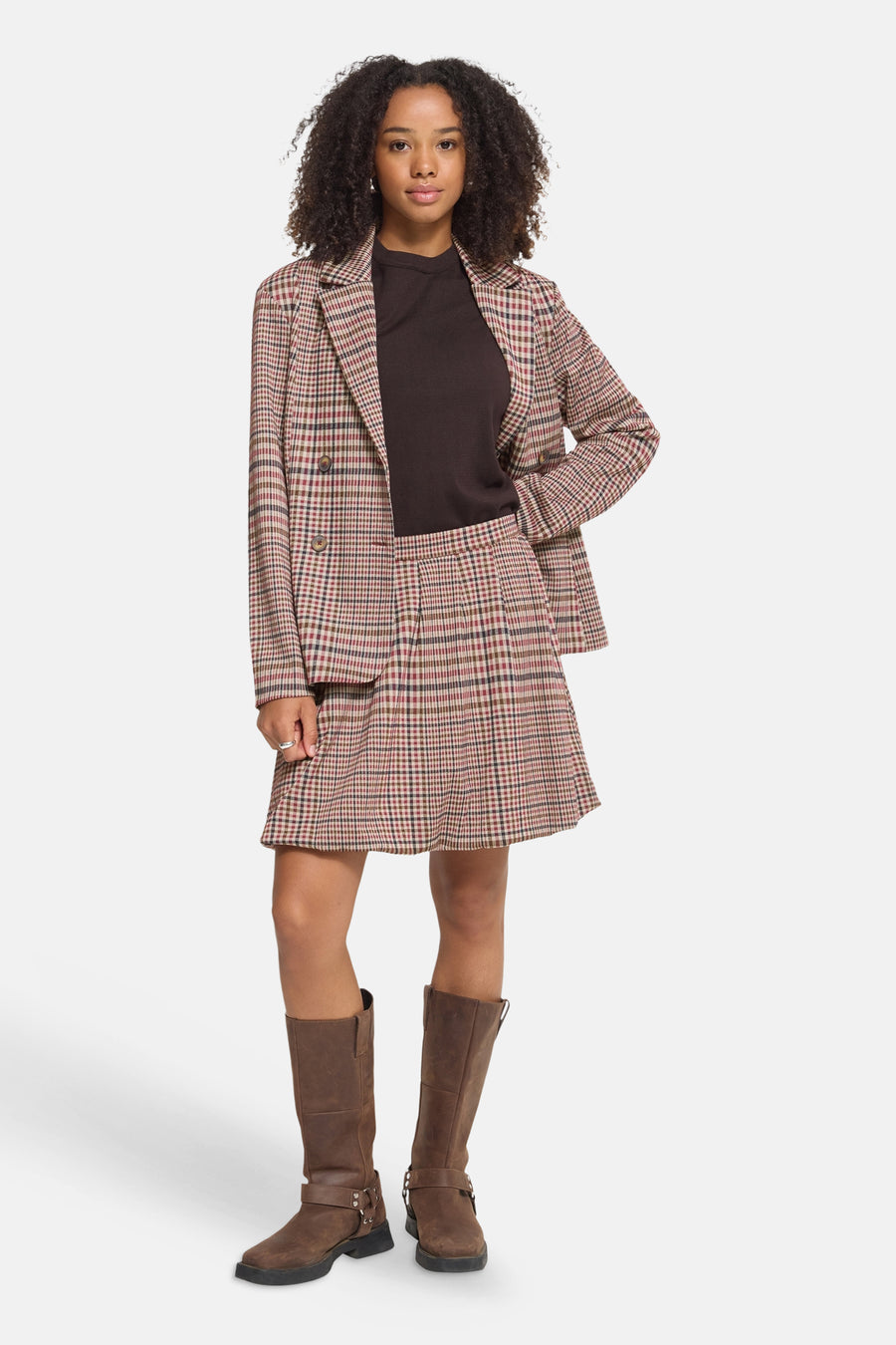 Multicolored plaid pleated mini skirt with matching blazer, worn with brown top and knee-high boots, full-length front view