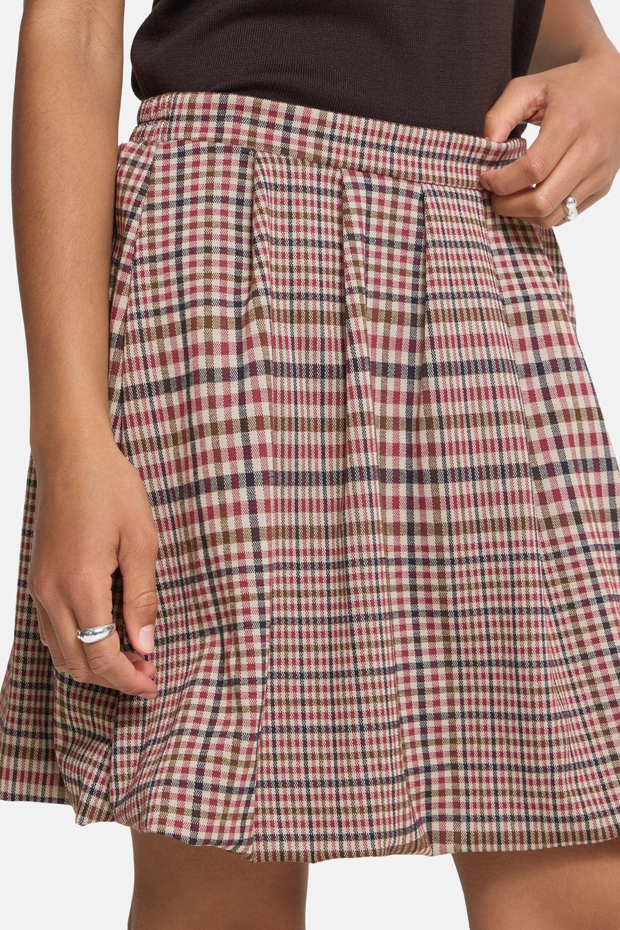 Multicolored plaid pleated mini skirt with red, brown, and cream checks, worn with dark top, side view