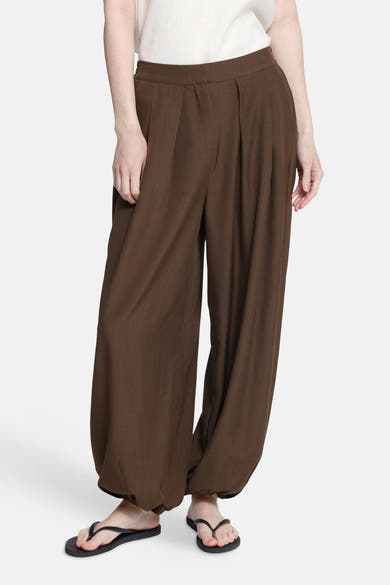 Brown wide-leg elastic waist trousers with pleated front and gathered ankles, worn with white top and black flip-flops, front view