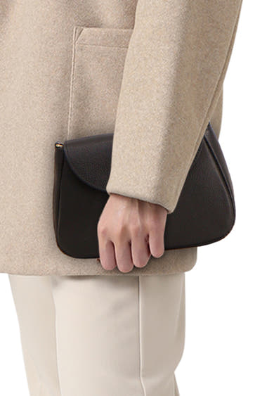 Sac à bandoulière noir en cuir par Access, porté à la main, avec un manteau beige et un pantalon écru.