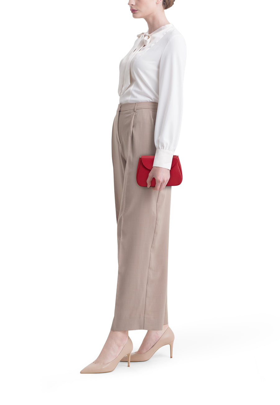 Sac à bandoulière rouge par Access®, porté avec un chemisier ivoire et un pantalon beige.