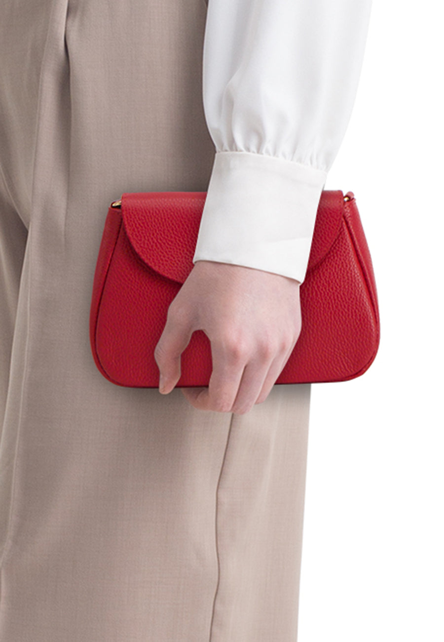 Sac à bandoulière rouge de Access, porté avec une chemise blanche et un pantalon beige.