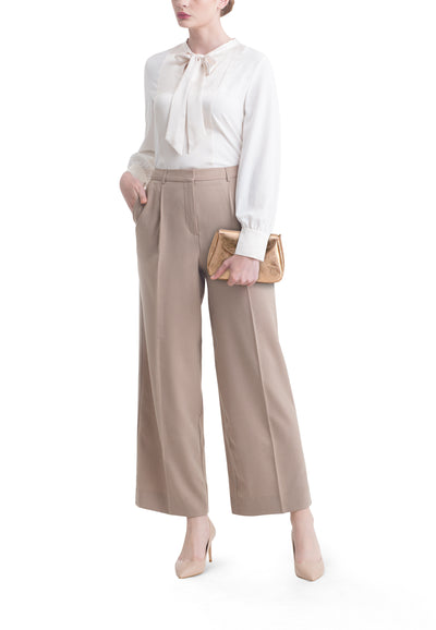 Gouden schoudertas van Access®, met een metallic afwerking en een overslagsluiting, gedragen met een blouse en een broek.