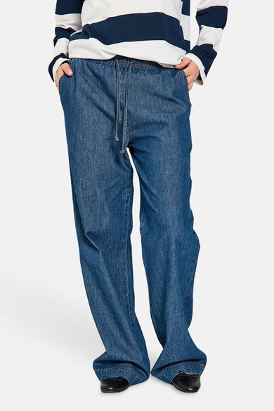 Pantalon en denim bleu moyen de FREEQUENT, avec cordon de serrage à la taille et porté avec un pull rayé.
