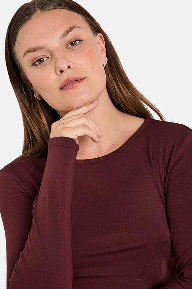 T-shirt bordeaux à manches longues de Freequent, porté avec des boucles d'oreilles argentées.