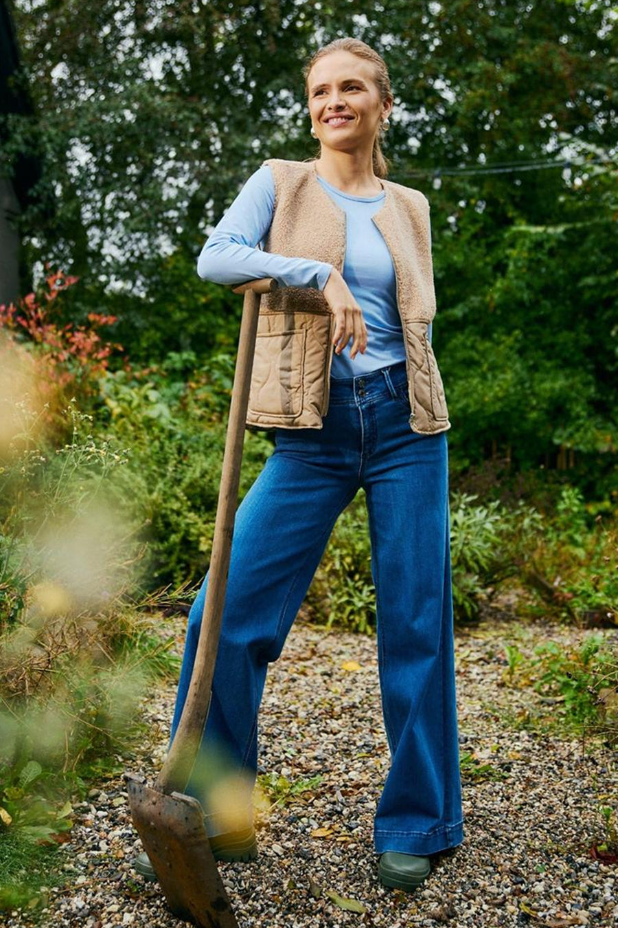 Mid blue denim wide-leg jeans by LOPEZ, worn with a beige quilted vest and light blue top, in a garden lifestyle shot