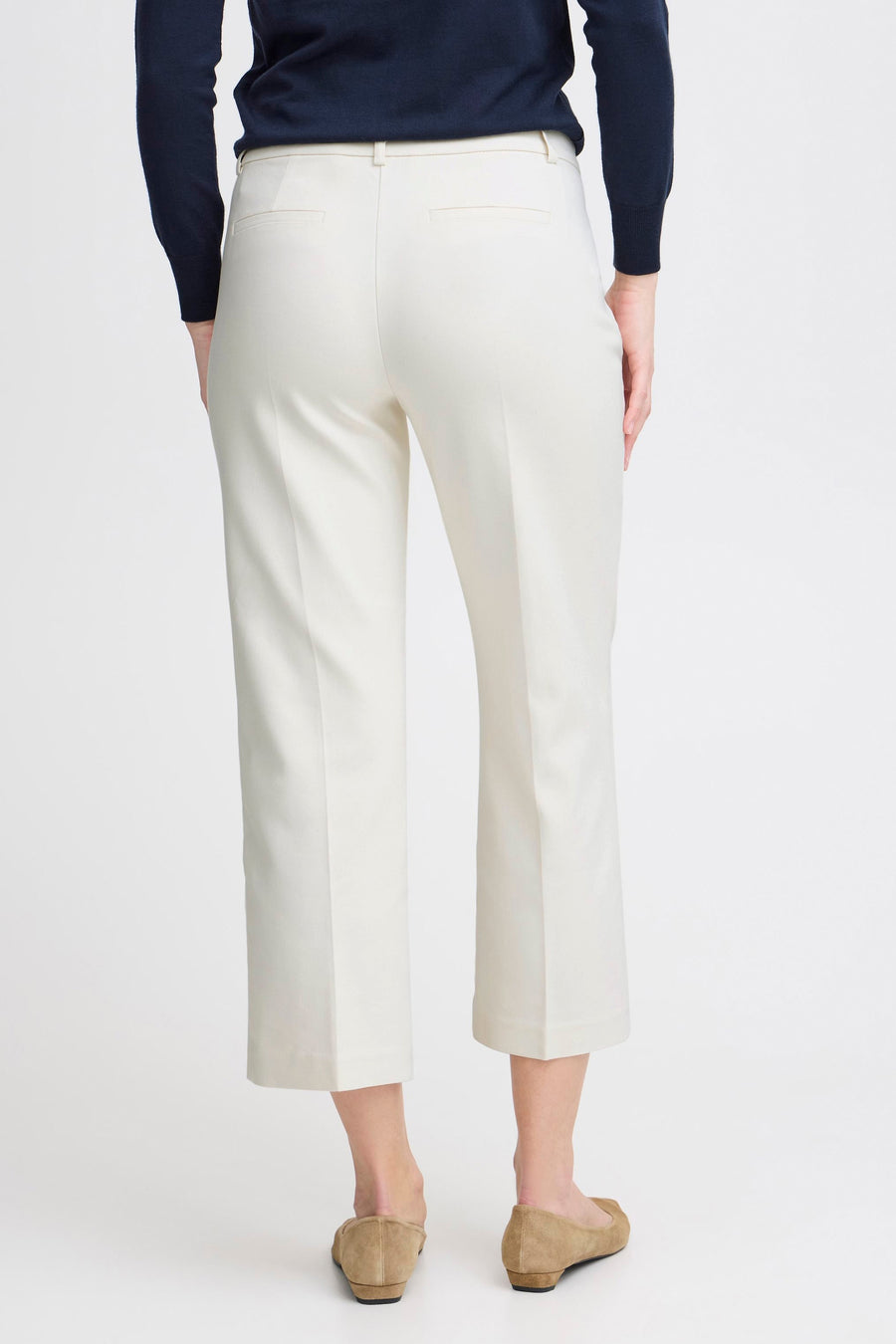 Pantalon chino blanc de Fransa, vu de dos, porté avec un pull bleu marine et des ballerines marron clair.
