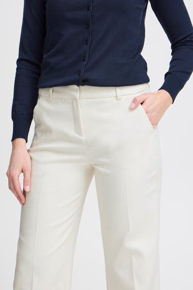 Chino beige de Fransa, porté avec un cardigan bleu marine, avec une main dans la poche.