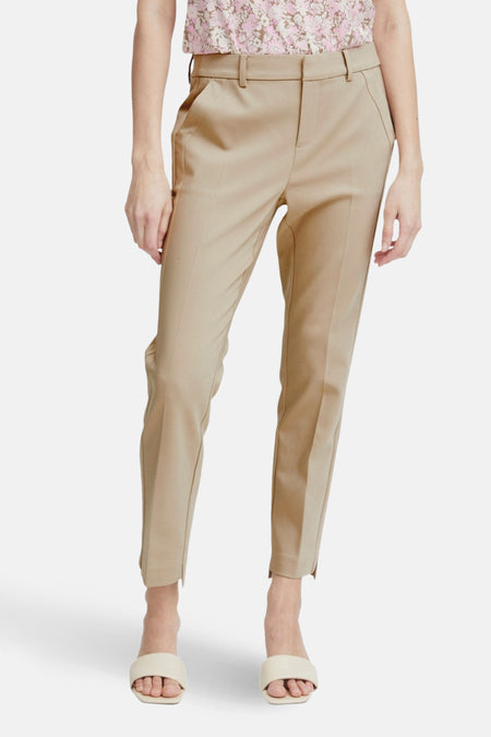 Chino beige par Fransa, avec poches et ourlets fendus, porté avec un haut fleuri et des mules crème.