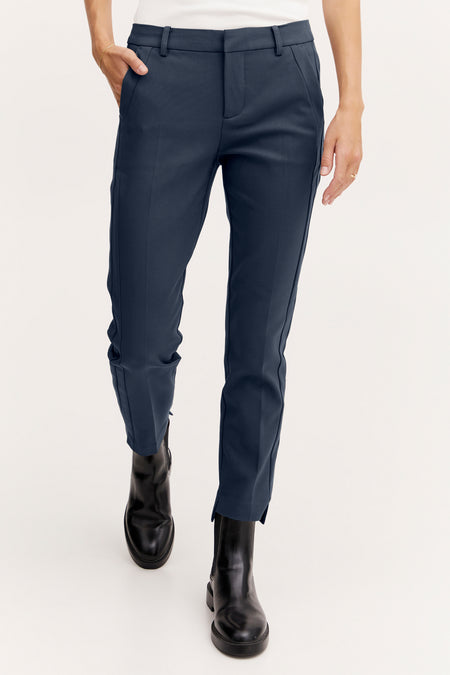 Chino beige van Frankrijk, gedragen met zwarte stiefels, een hand in de zak.