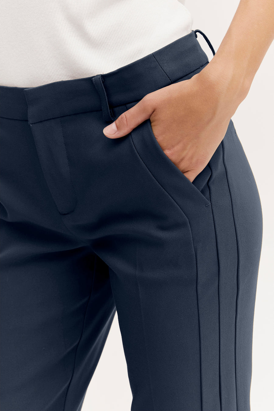 Pantalon chino bleu marine de Fransa, avec une main dans la poche, associé à un haut blanc.
